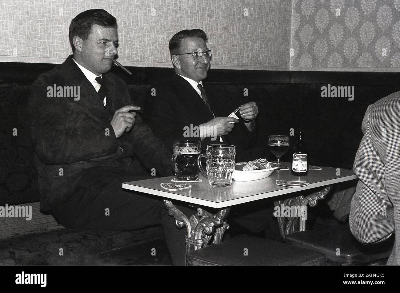 1960s, historical, two well-dressed men sitting in a corner of a bar or pub, drinking beer, with a bottle of Dutton's Pale Ale on the table, England, UK. Stock Photo