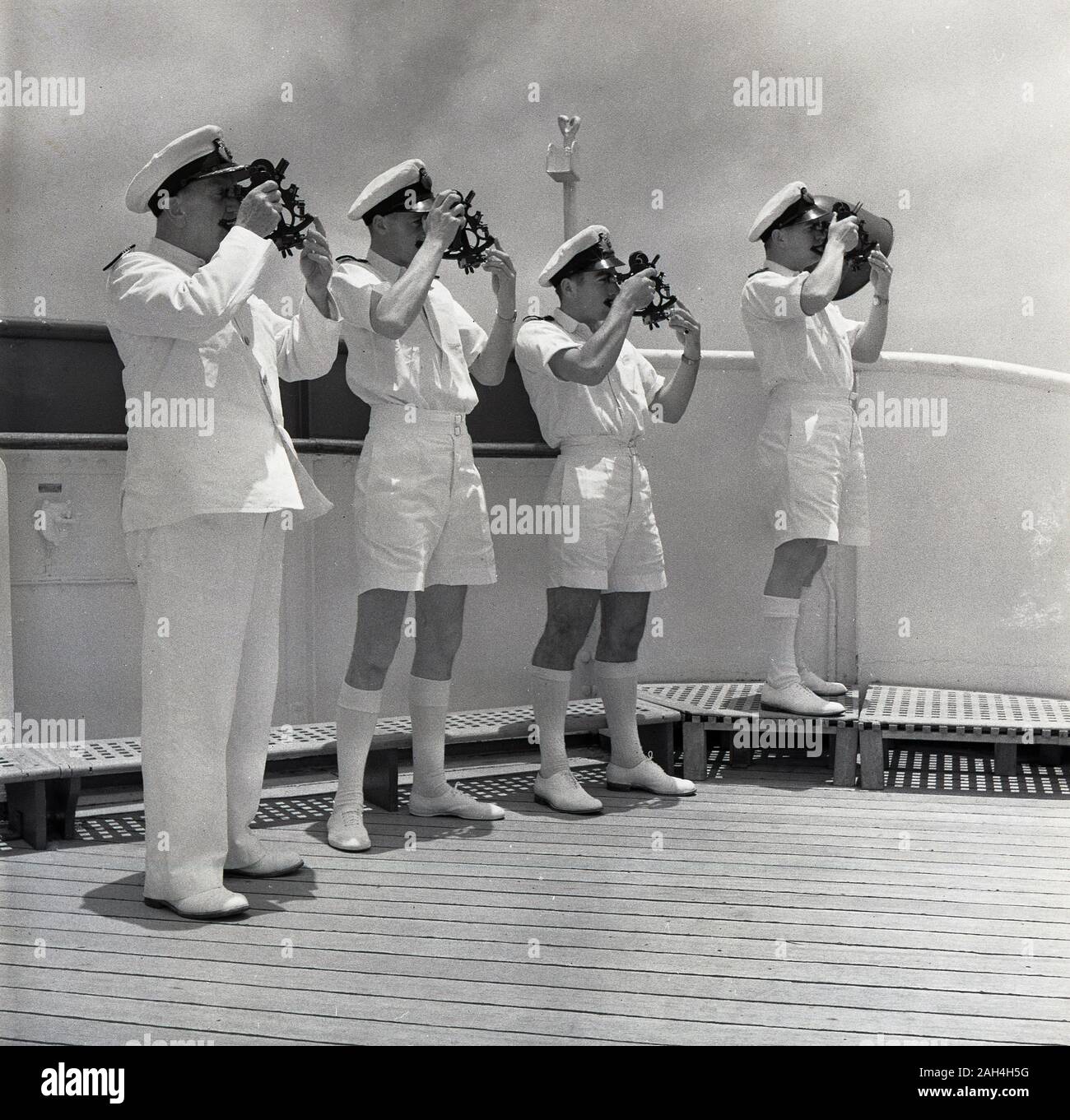 1950s, historical, a captain and three uniformed crew standing outside on the deck of their steamship using traditional measuring instruments, sextants, to navigate the ship's course. Sextants are maritime measuring instruments used to determine the angle between the horizon and a celestial body such as the sun, moon or a star. Stock Photo
