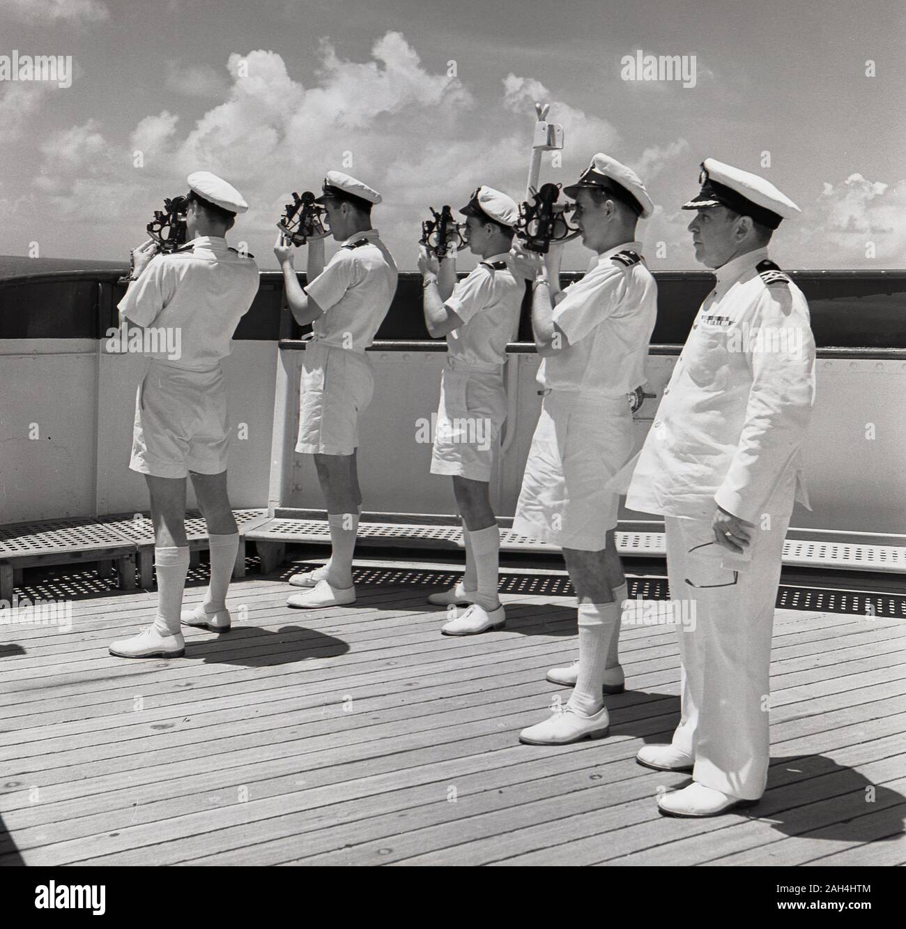 1950s, historical, a group of four uniformed ship's navigators standing out on the deck of a steamship using sextants, overseen by ship's captain. Sextants are maritime measuring instruments used to determine the angle between the horizon and a celestial body such as the sun, moon or a star. Stock Photo
