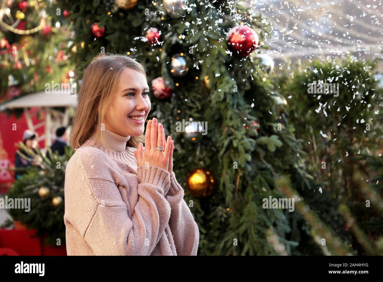Happy girl laughing and enjoys the snow during standing on New Year tree background during traditional festival Journey to Christmas Stock Photo