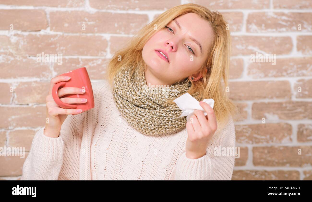 Cold and flu symptoms. Sick woman with sore throat drinking cup of warm tea. Pretty girl with nasal cold suffering from headache. Cute woman caught terrible cold virus. A tea cure. Stock Photo