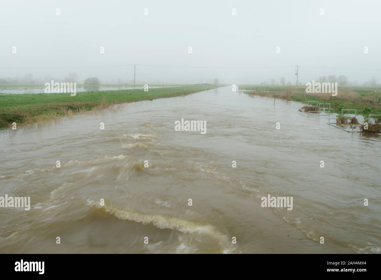 A turbulent drainage canal over flowing its banks in flood. Stock Photo