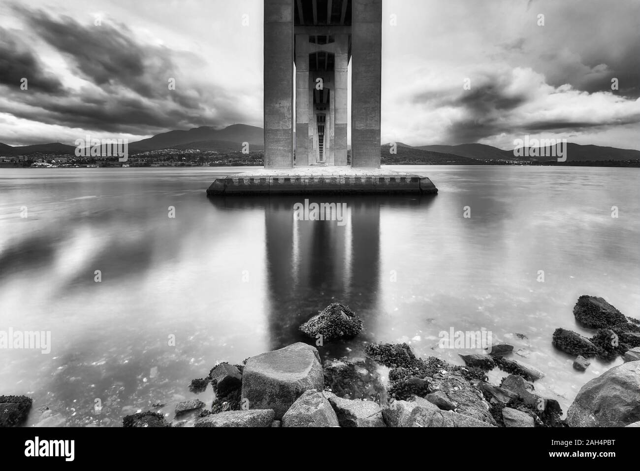 High contrast black white view from underneath the Tasman bridge across Derwent river in Hobart at sunrise when clouds reflect in still waters. Stock Photo