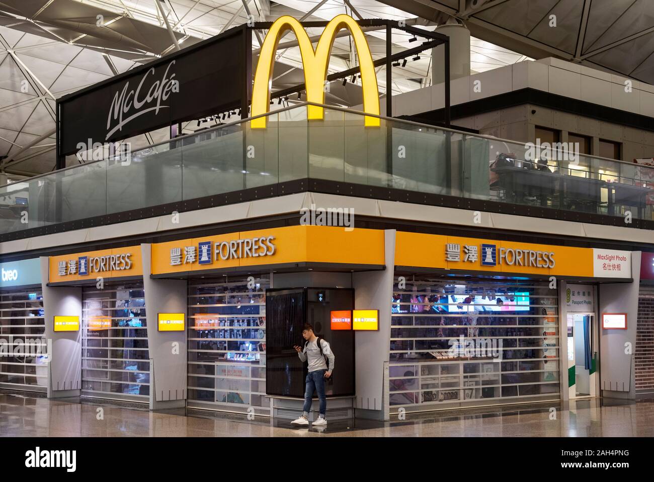 A man stands under a large McDonald's fast-food restaurant logo and Hong Kong Electricity Group, Fortress store at the Hong Kong international airport. Stock Photo