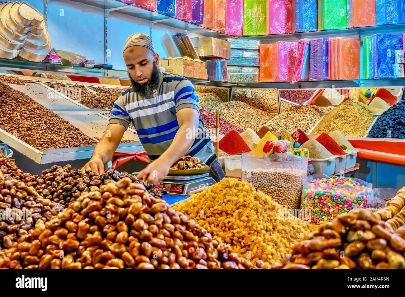 Marrakech, Morocco - October 22, 2015. A Moroccan man at work in a public market stall which sells dates, nuts, spices, candy, and gift boxes. Stock Photo