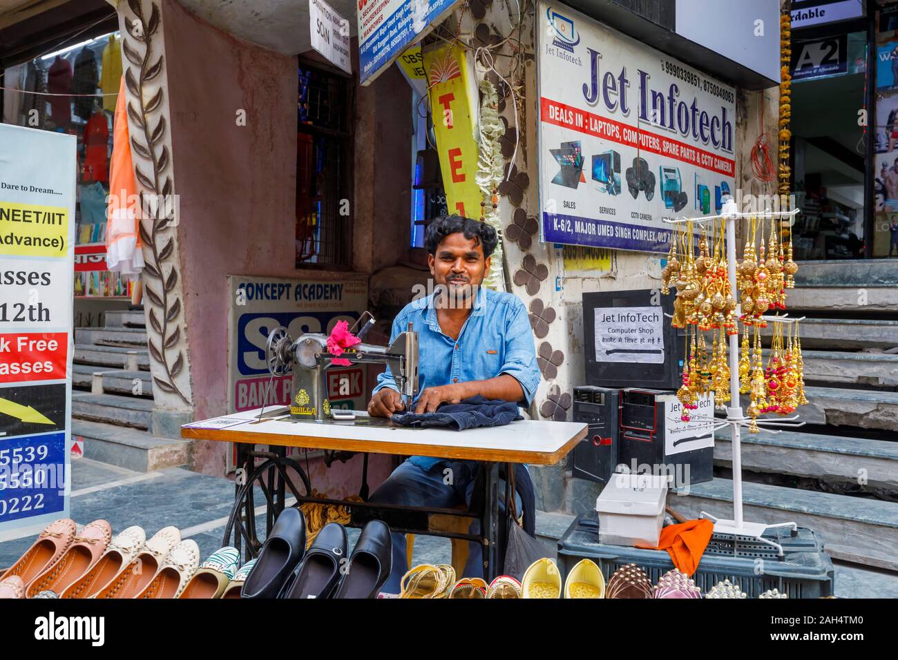 Street scene in Mahipalpur district, a suburb near Delhi Airport in New Delhi, capital city of India: local man working with a manual sewing machine Stock Photo