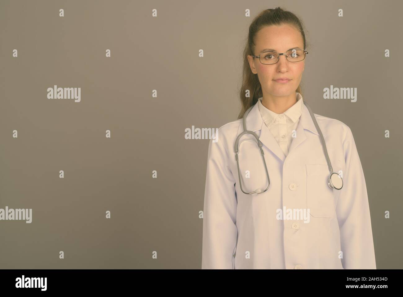 Studio shot of young beautiful woman doctor wearing eyeglasses against ...