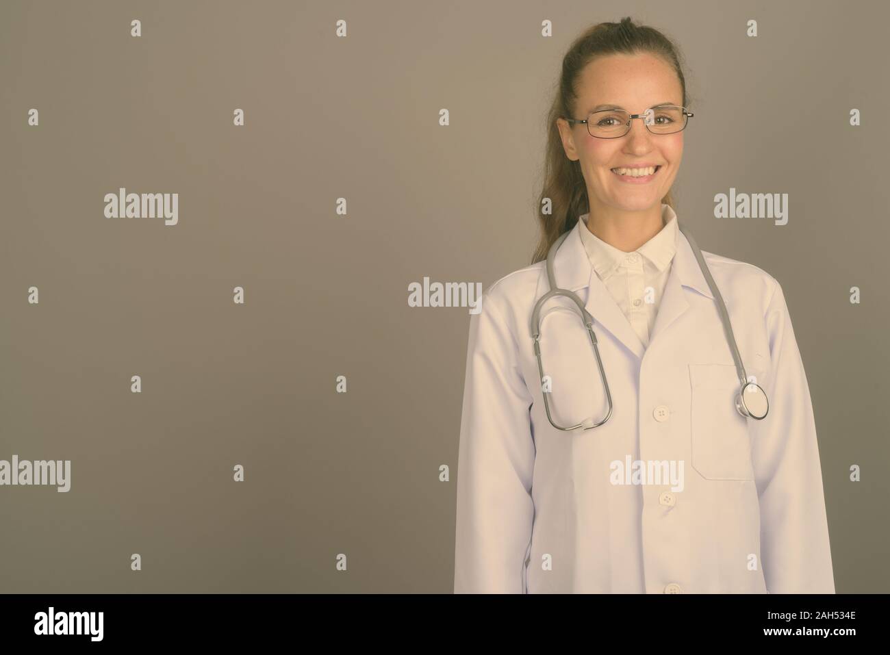 Studio shot of young beautiful woman doctor wearing eyeglasses against ...