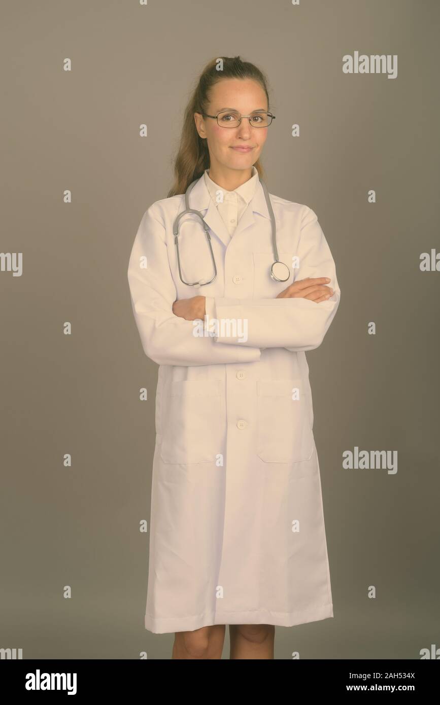 Studio shot of young beautiful woman doctor wearing eyeglasses against ...