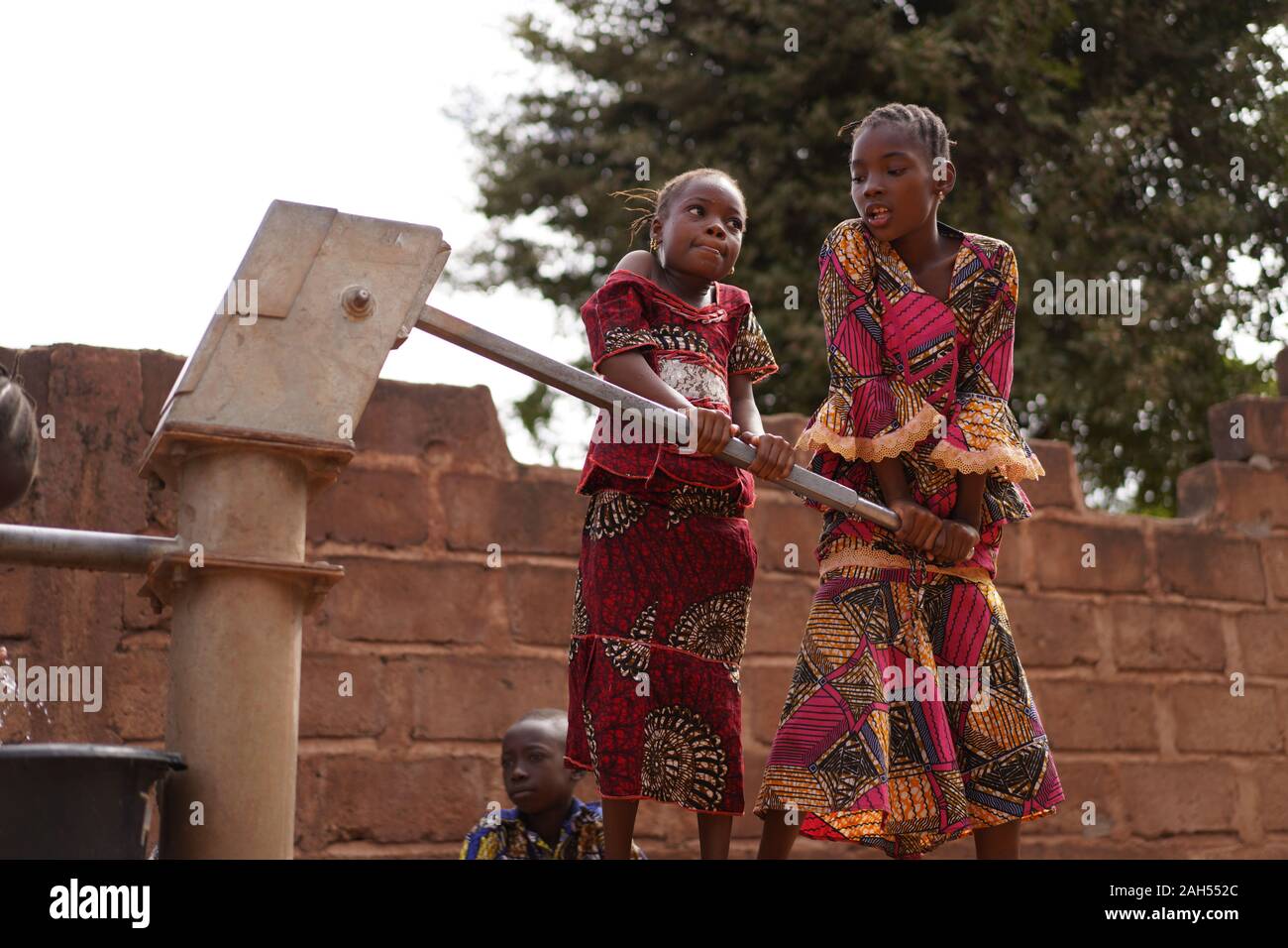 Young Girls Helping Each Other Pumping Water At An African Village Borehole Stock Photo