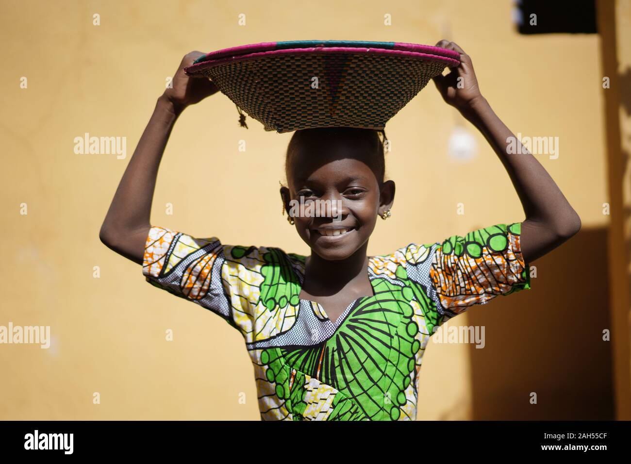 Cute African Girl Carrying a Couloured Handmade Straw Basket On Her Head Stock Photo