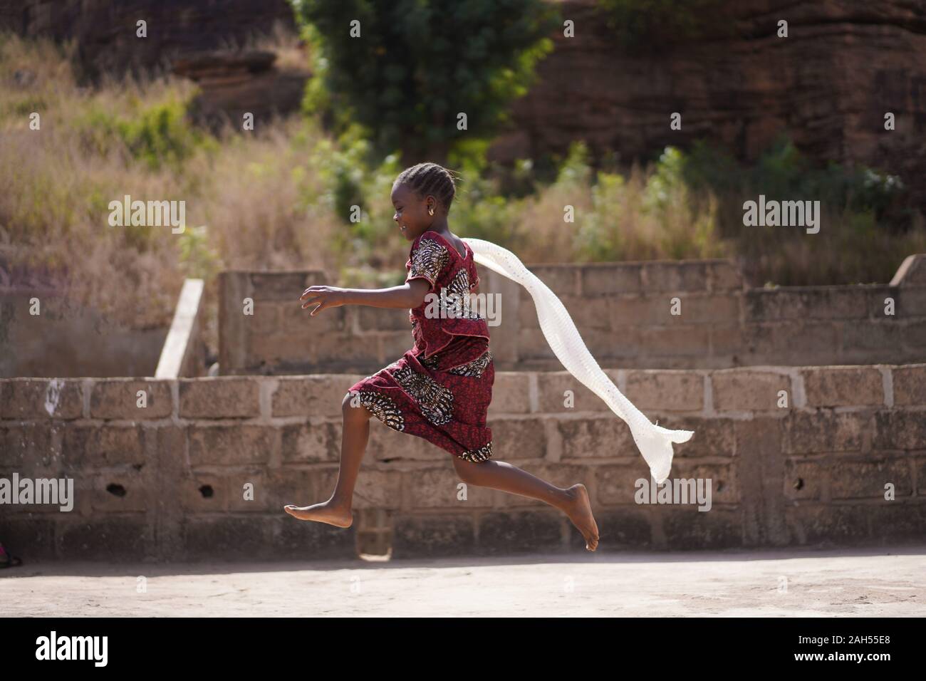 Colourfully Dressed Little African Girl Running With Her White Scarf Flowing In The Wind Stock Photo