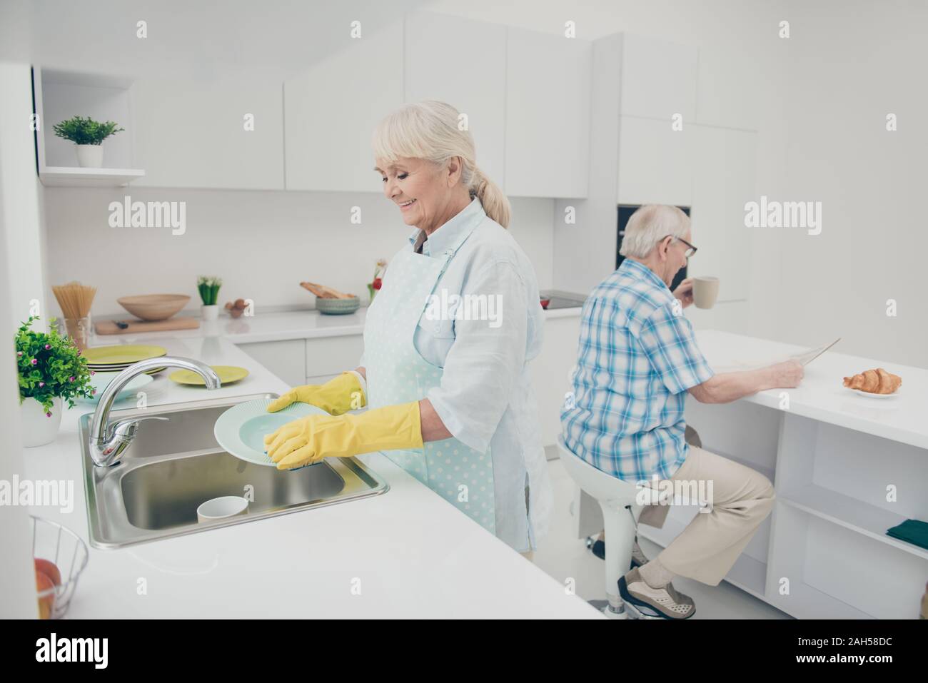 Portrait of nice cute old lady hold hand, polishing drying plates wet hands enjoy house work have kitchenwear stand indoors Stock Photo