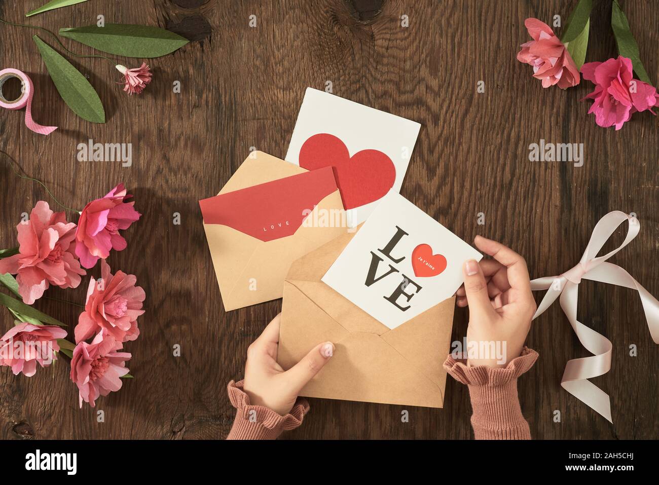 Valentine card on wood background with color paper flowers, ribbon. Flatlay, top view. Stock Photo