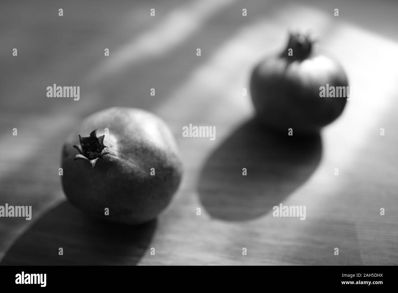 Two whole ripe pomegranate on the wooden sunny table, bw photo. Stock Photo