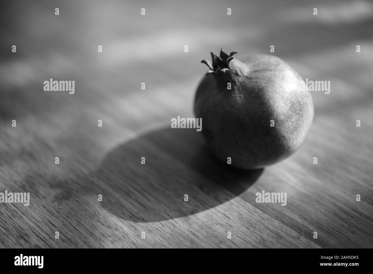 Whole ripe pomegranate on the wooden sunny table. Stock Photo