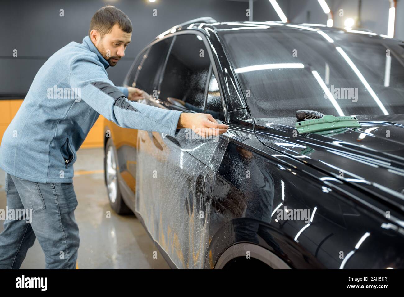 Car service worker sticking anti-gravel film on a car body for protection at the detailing vehicle workshop Stock Photo