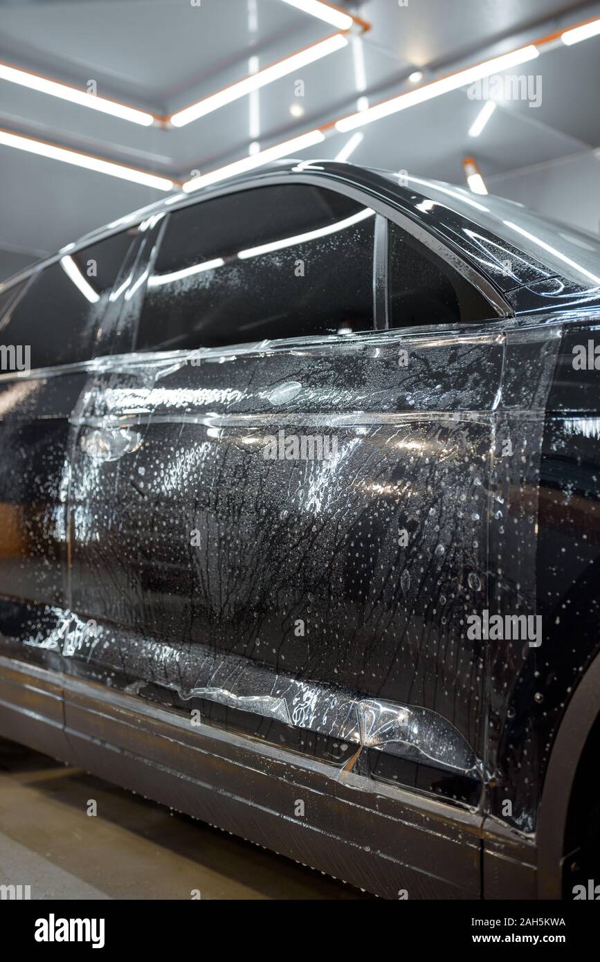 Wet car body during a protective film applying at the vehicle service garage Stock Photo