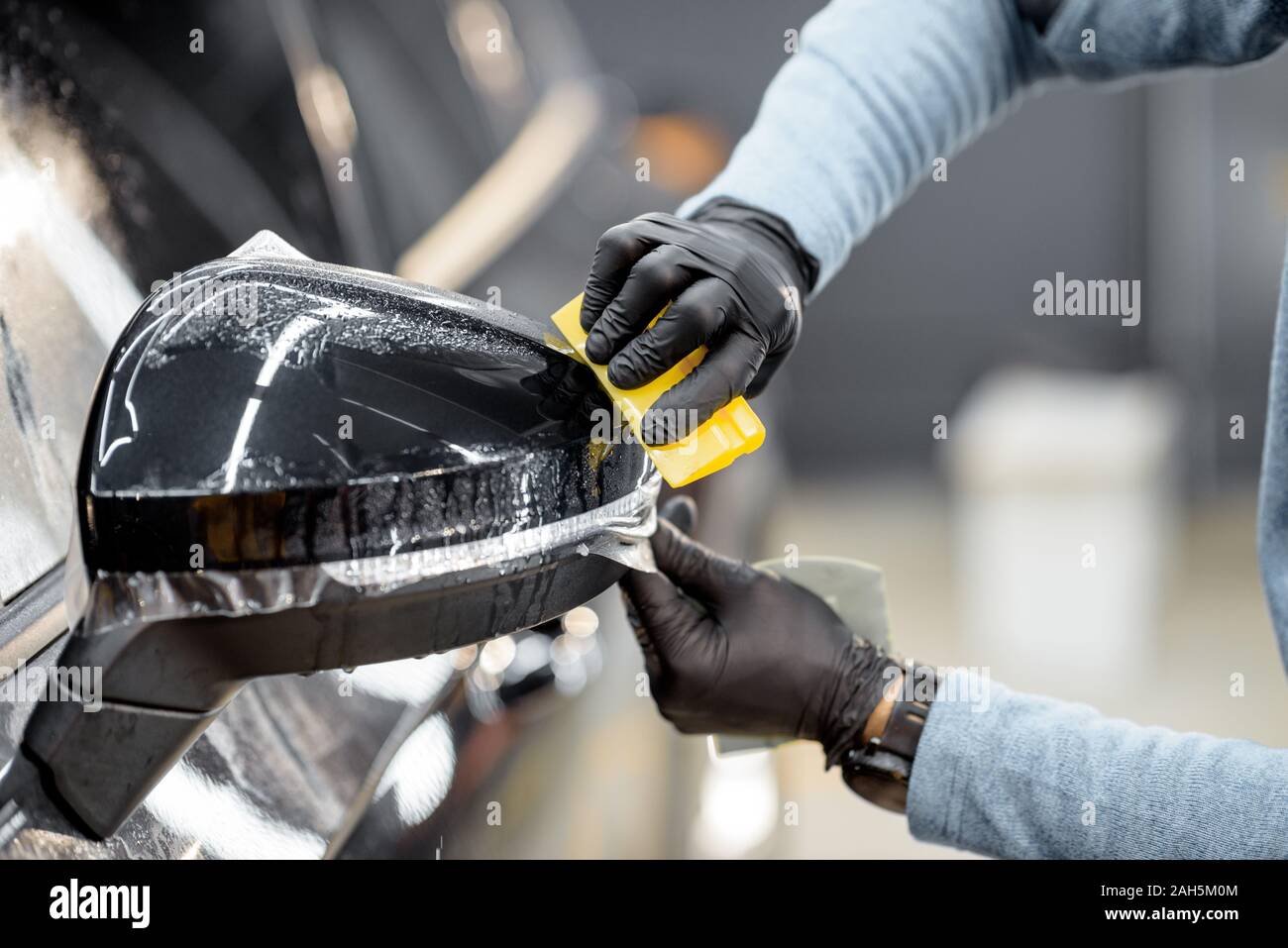 Man applying sticking protective film on a car mirror at the vehicle service station, clloseup