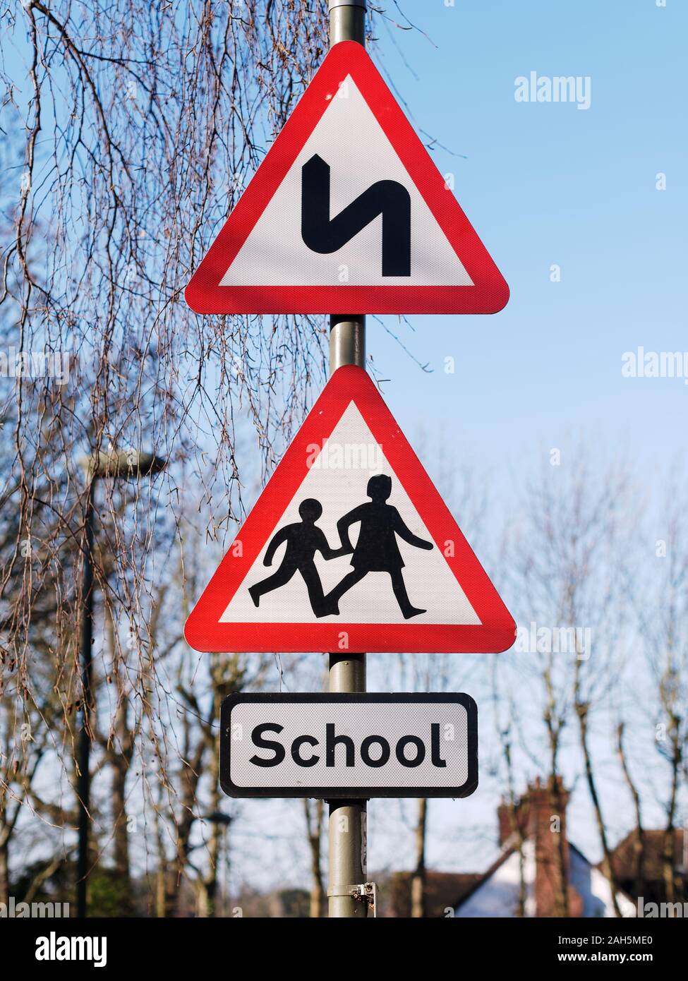 Double bend first to left sign and school children crossing sign. UK road traffic triangular warning signs Stock Photo