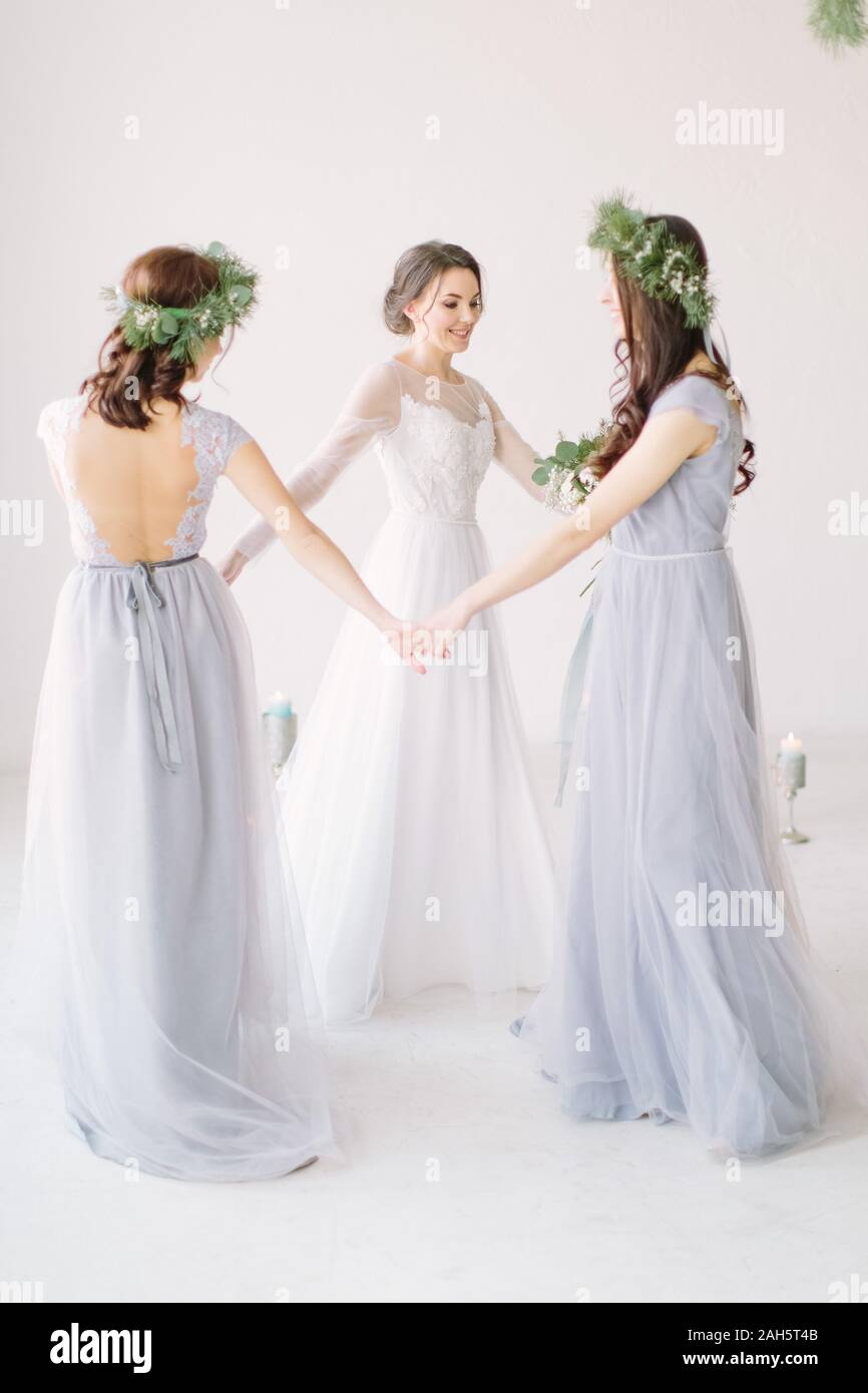 Pretty bride and bridesmaids holding hands and dancing in white studio ...