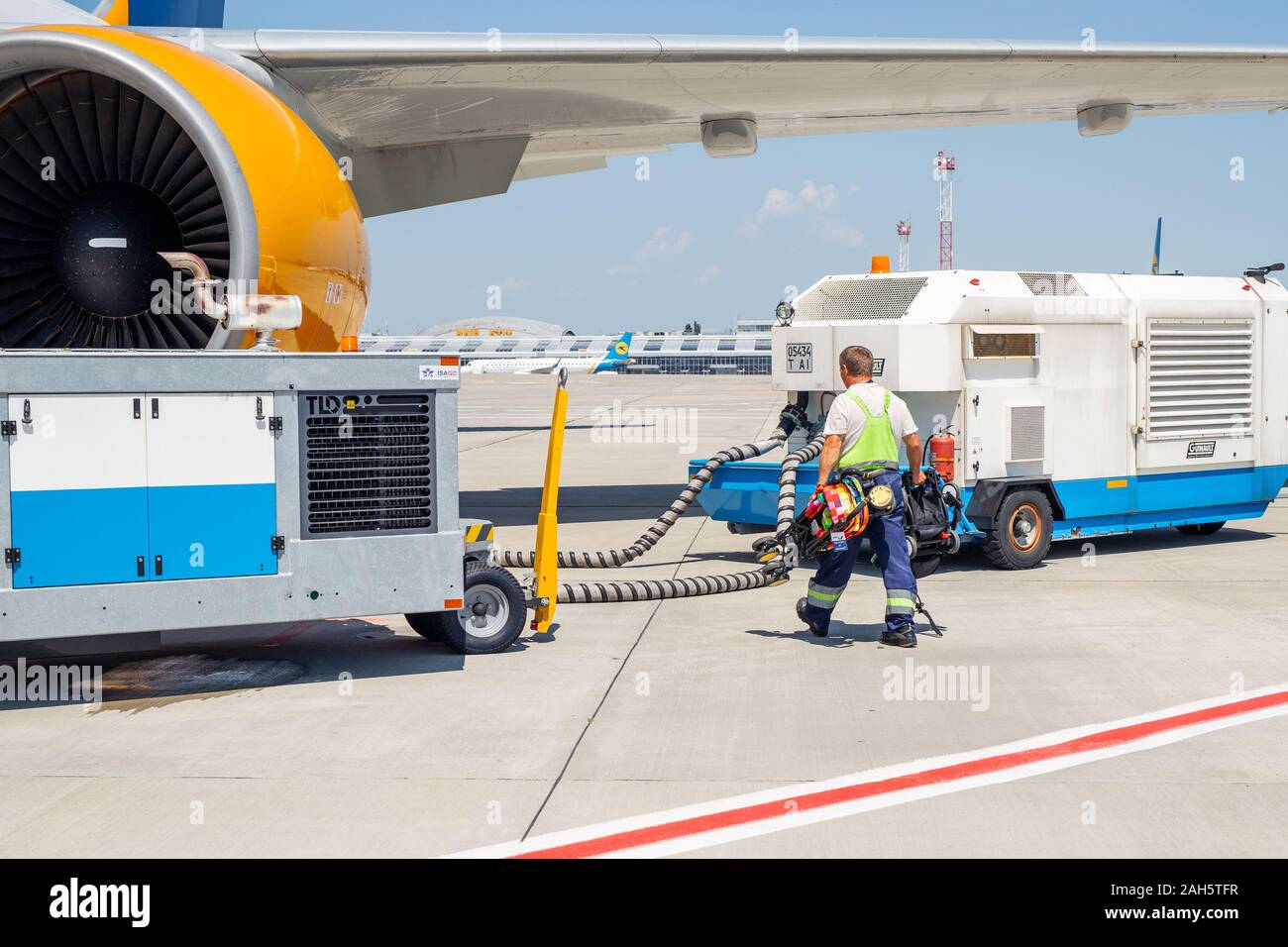 Kyiv, Ukraine - June16th, 2019: Big modern commercial plane parked on airport runway and connected to ground supply power unit. Crew worker stuff Stock Photo