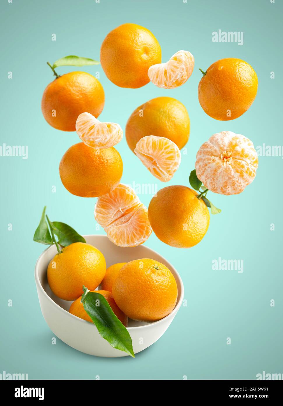 Tangerines flying over blue background, in a bowl isolated from the bottom, fresh seasonal tangerines Stock Photo