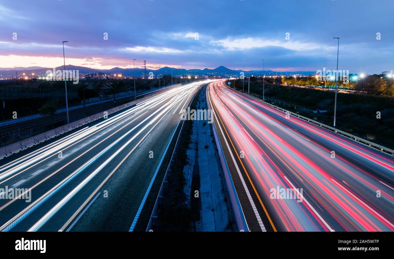Highway at sunset, vehicles driving in two directions leaving trails of light, return home from work Stock Photo