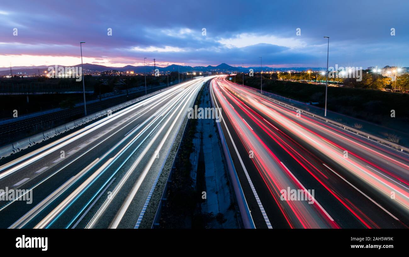 Highway at sunset, vehicles driving in two directions leaving trails of light, return home from work Stock Photo