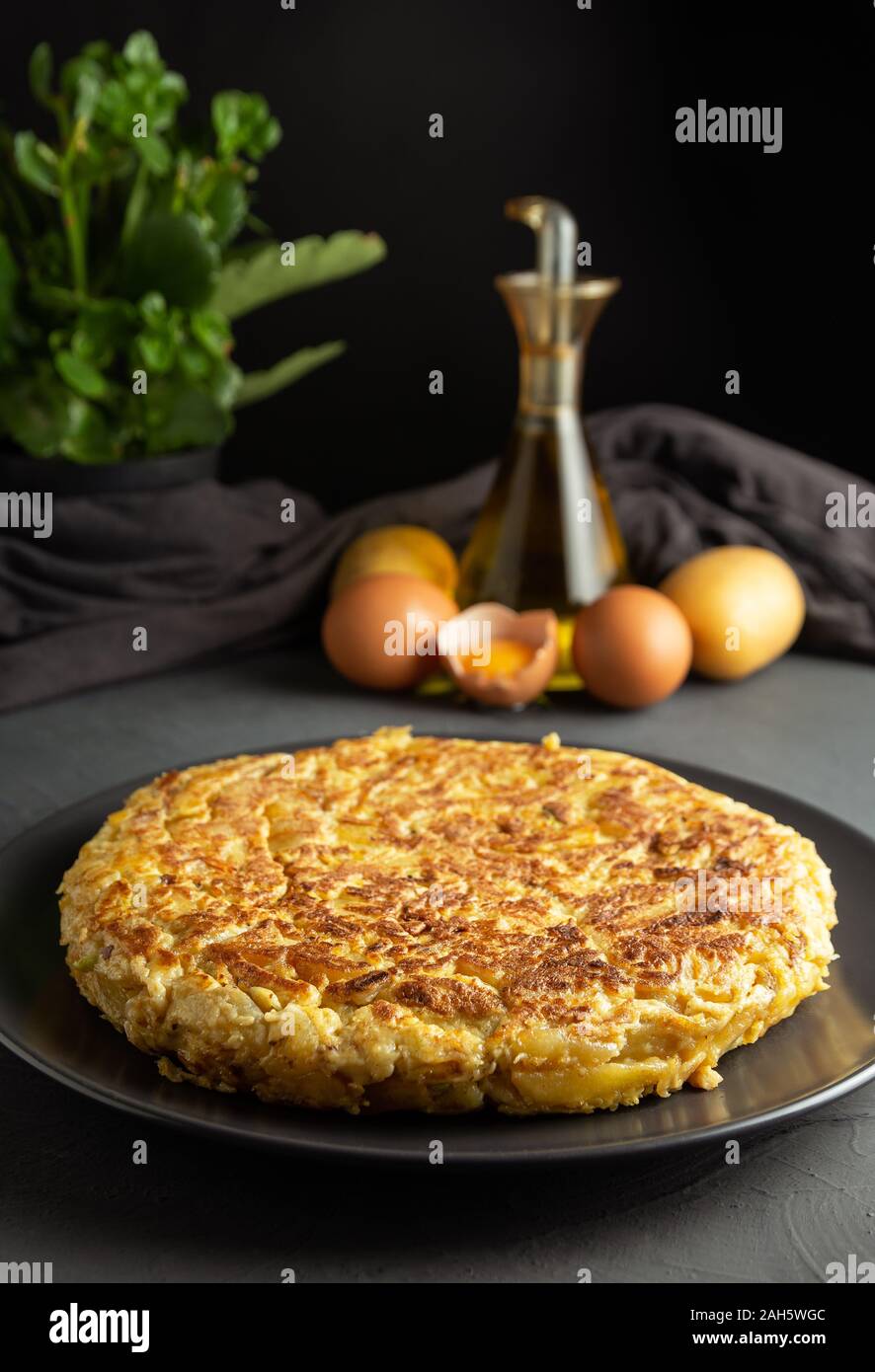 Potato omelet on dark wooden background, ingredients for preparation in the background Stock Photo