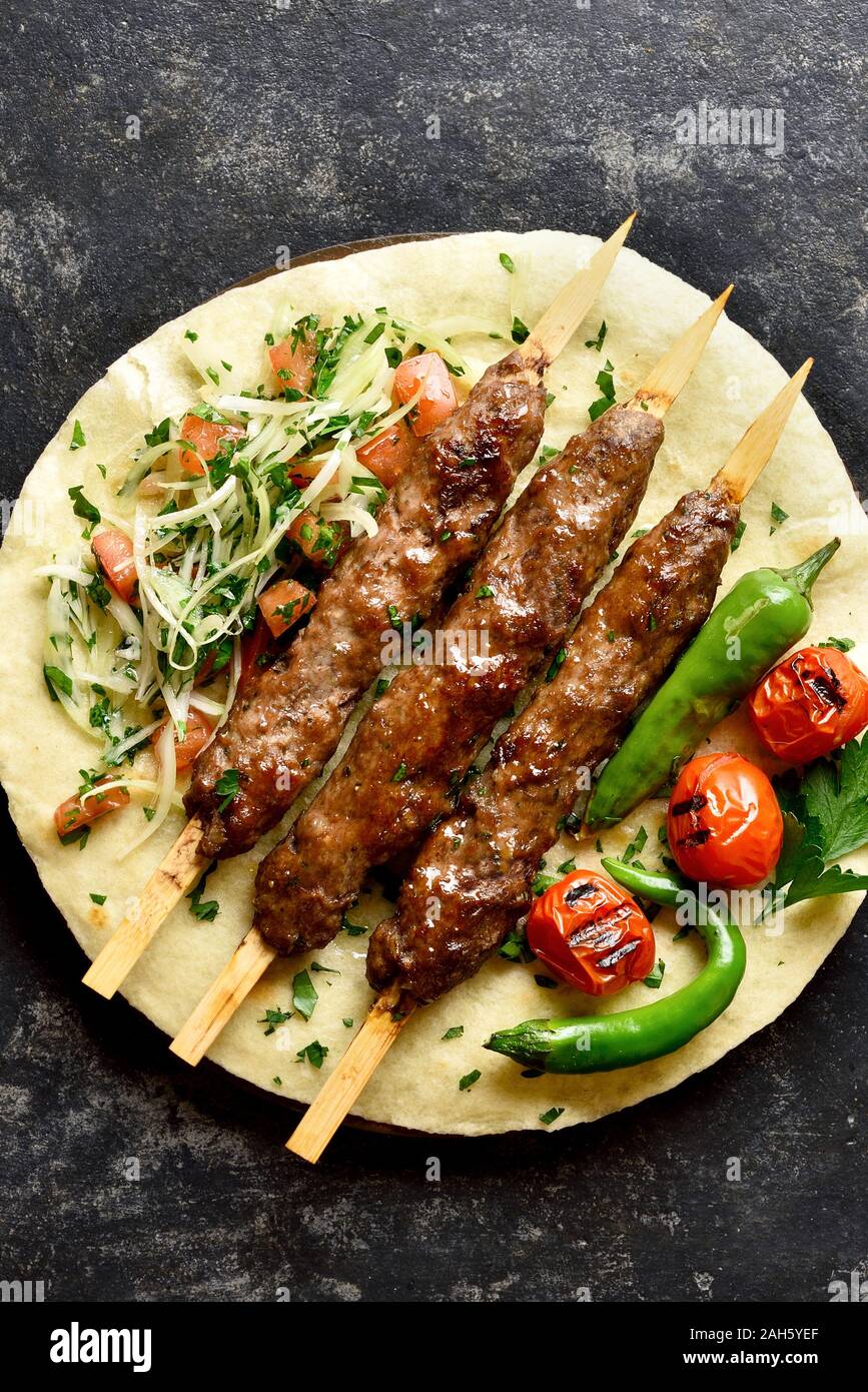 Turkish Adana Kebab with fresh vegetables on flatbread over black stone background. Top view