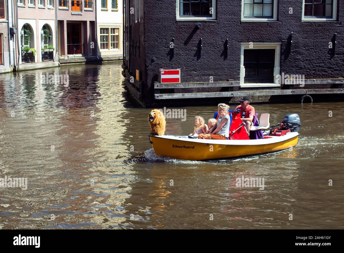 Close up view of a family riding a small, yellow, open boat in canal doing a tour at Armbrug bridge area in Amsterdam. It is a sunny summer day. Stock Photo