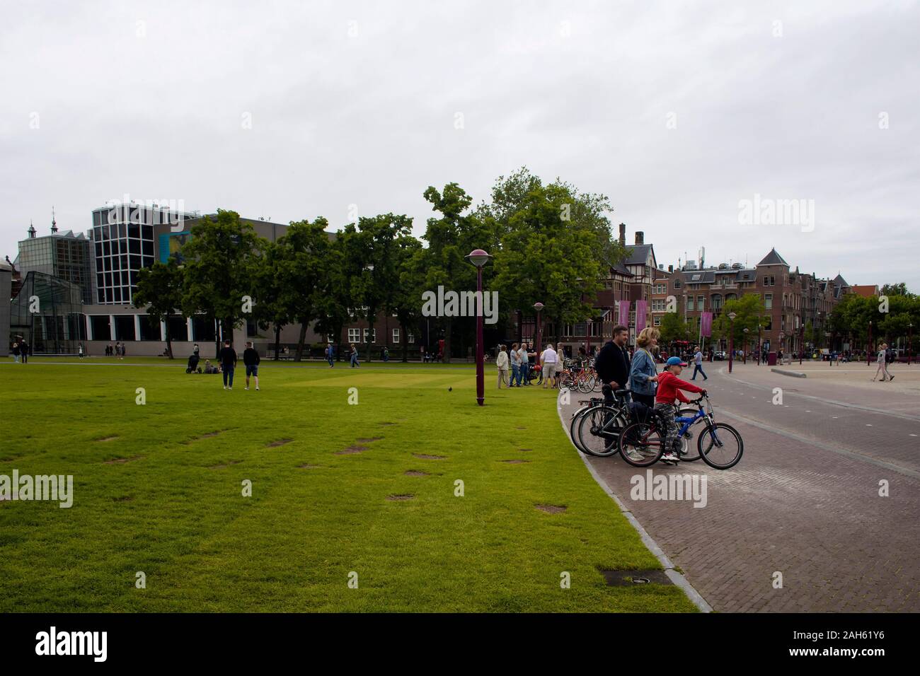 View of people at hanging out and a family riding bicycles at Museum Quarter (square) in Amsterdam. It is a summer day with cloudy sky. Stock Photo