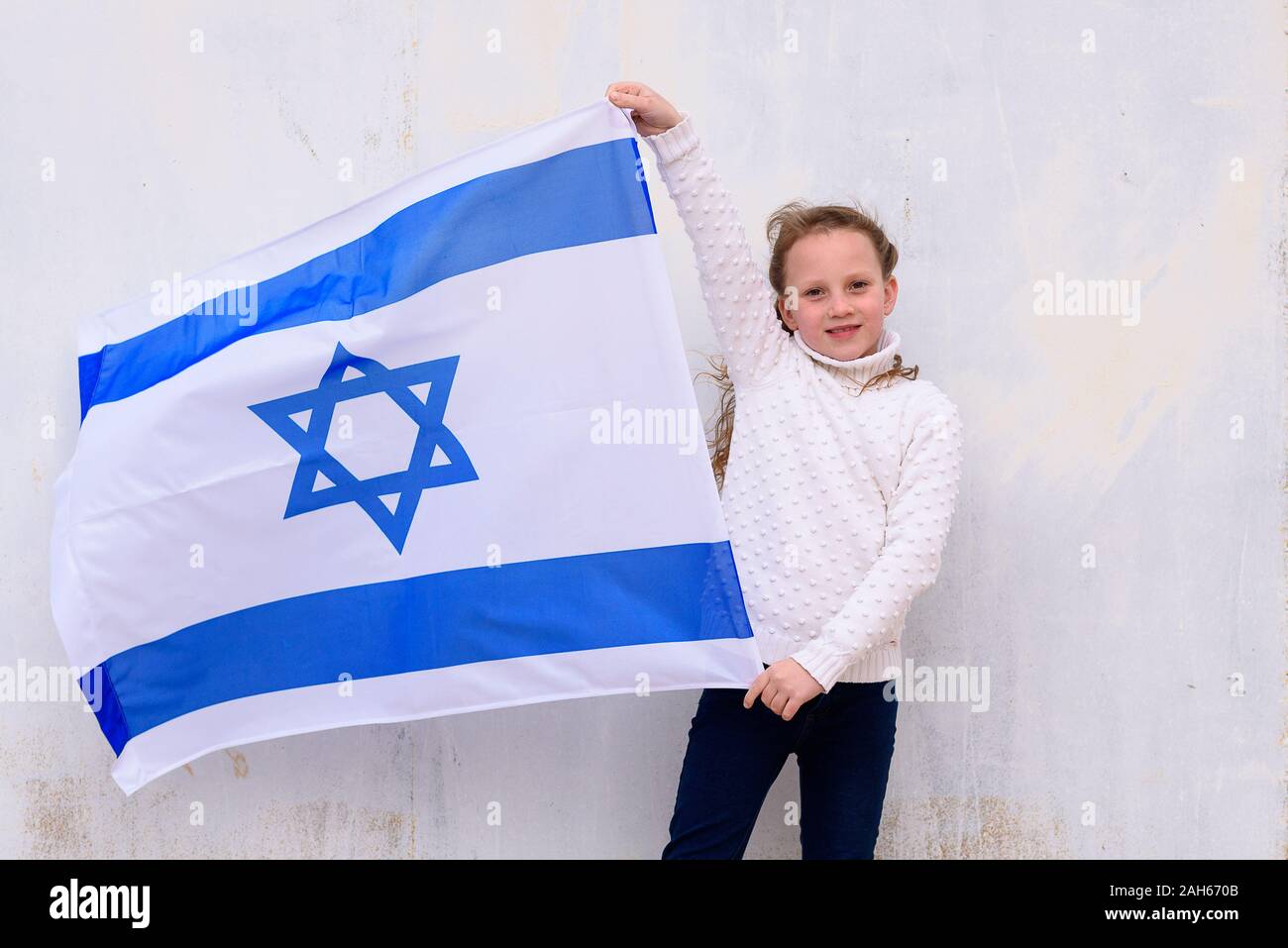 Little patriot jewish girl standing and enjoying with the flag of Israel on white wall background.Memorial day-Yom Hazikaron, Patriotic holiday Independence day Israel - Yom Ha'atzmaut concept Stock Photo