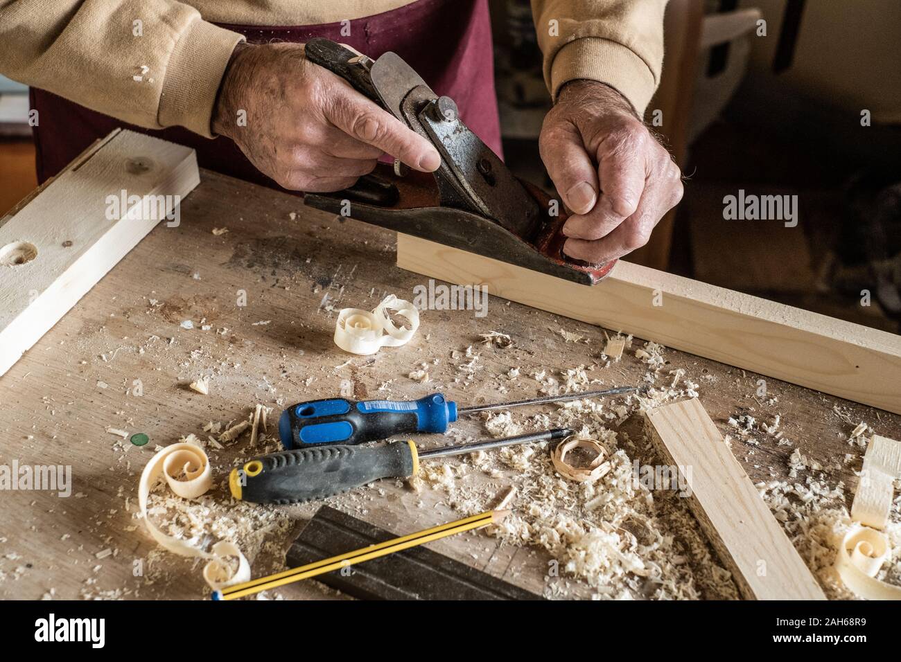 Carpenter man scraping curled wood scraps with hand plane tool and wooden plank. Stock Photo