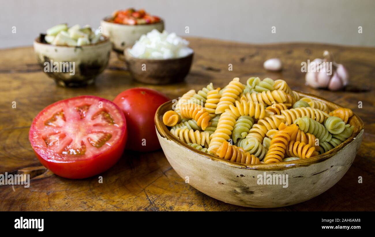 Fresh ingredients for cooking: pasta, tomato, red pepper, onion, eggplant and garlic over old wooden table background. Stock Photo