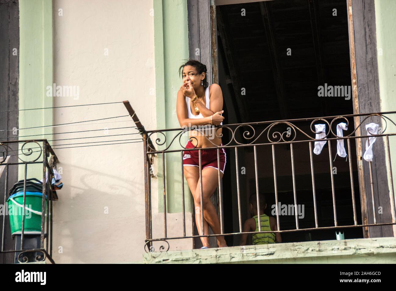 People of Havana Series - An attractive, single, Cuban woman, in her 20s, learning over the balcony of her apartment. Stock Photo