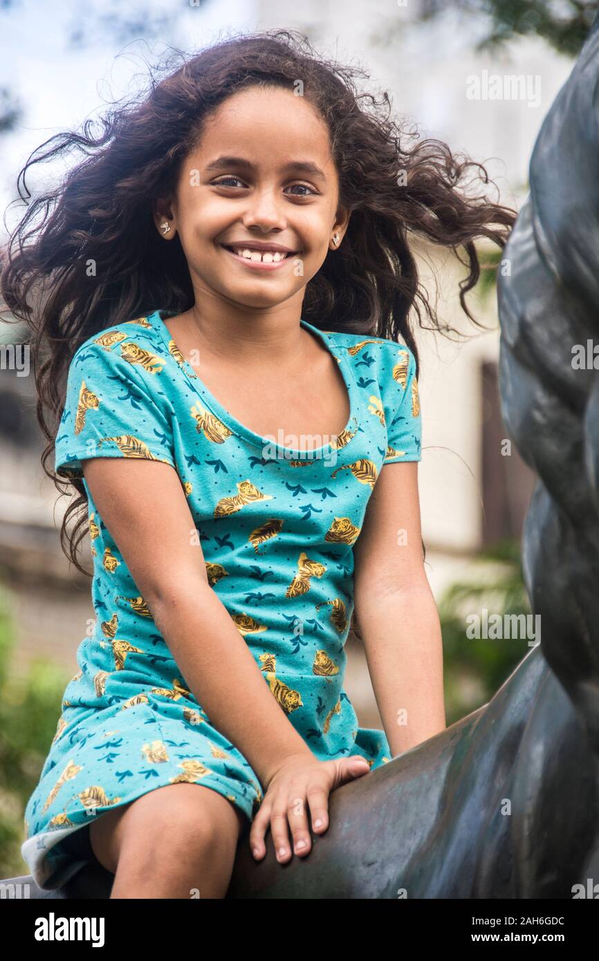 People of Havana Series - A cute little nine year old, Cuban girl sitting on a statue of a horse. Stock Photo