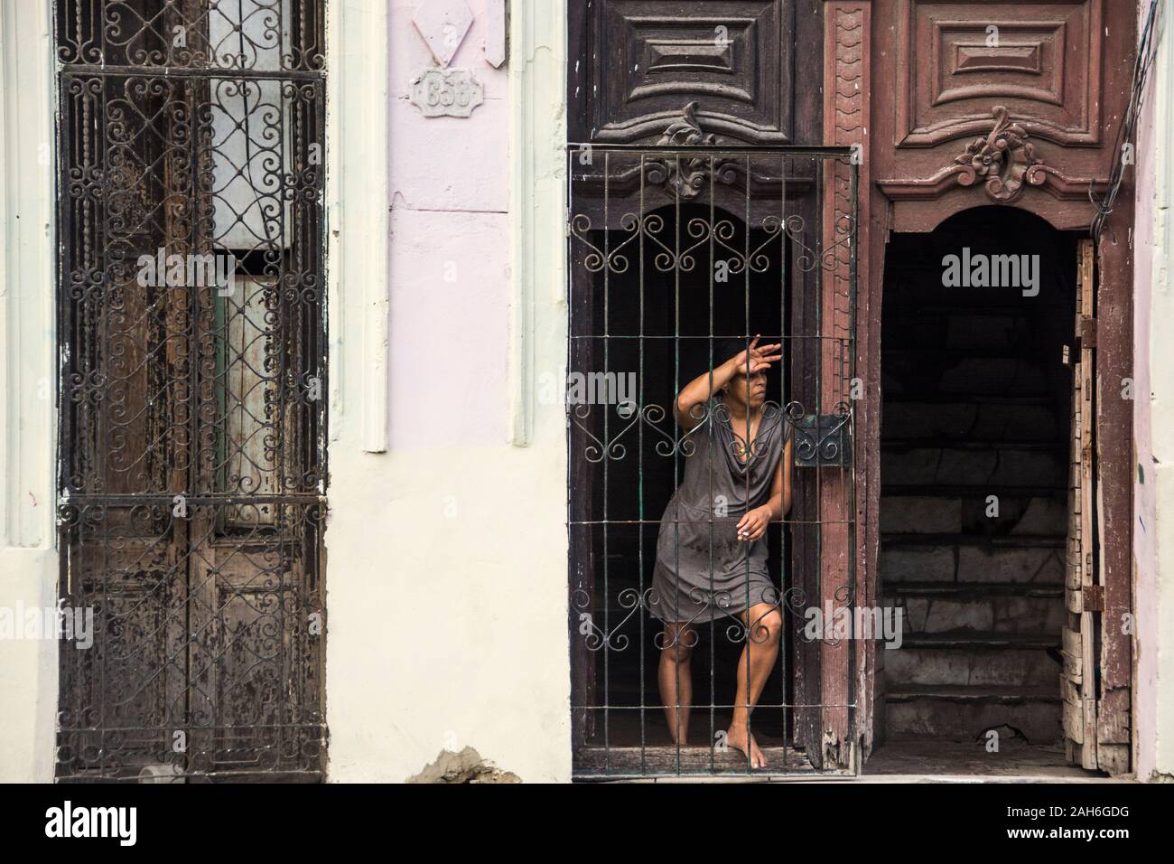 People of Havana Series - A woman in her late 20s, early 30s, looking at the world through her security door. Stock Photo