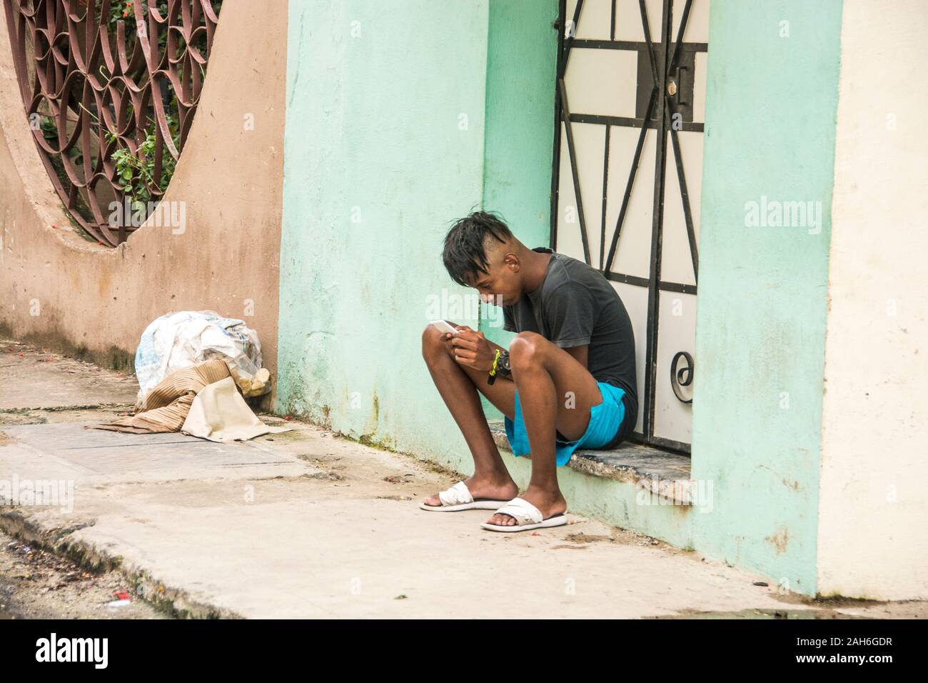 People of Havana Series - A young, teen ager, checks out his cell phone, while sitting in front of his house. Stock Photo