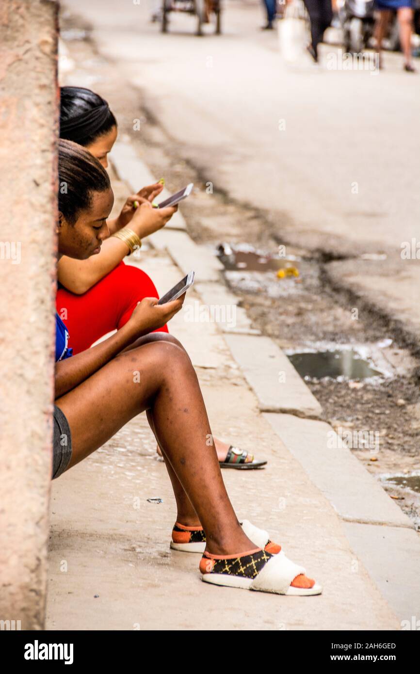 People of Havana Series - Two young, Cuban girls talking on their cell phones, while sitting outside their homes. Stock Photo