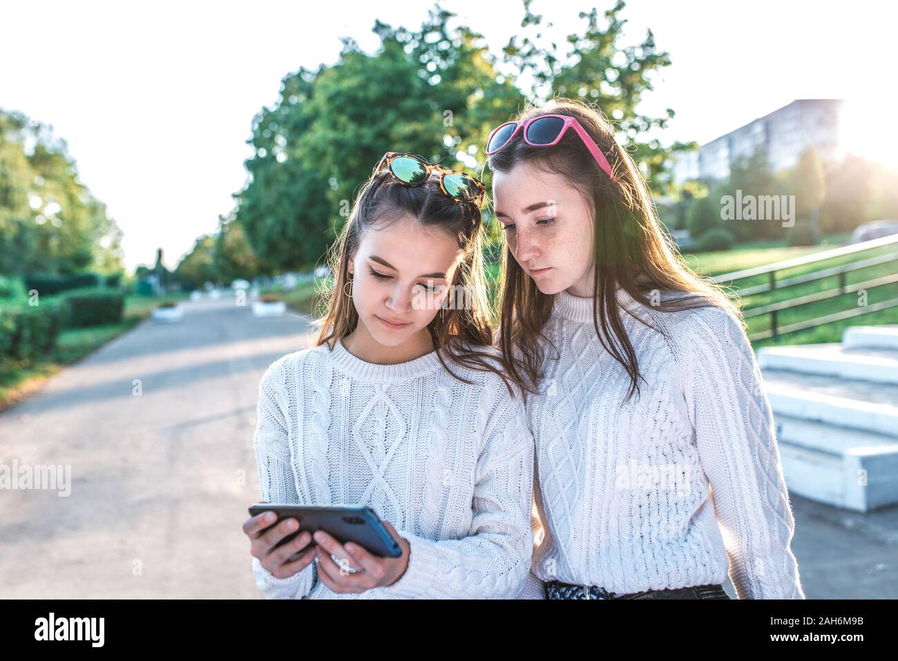 Two girls schoolgirls girlfriends 12-15 years old, watching video phone,  summer city after lessons school and college, autumn warm sweaters. Casual  Stock Photo - Alamy