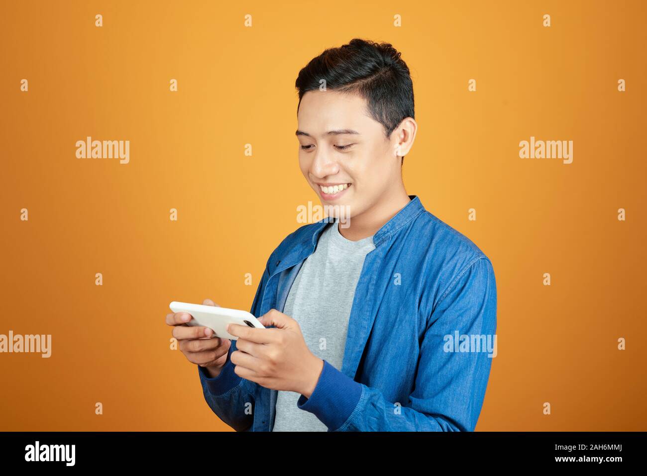 Smiling young good looking Asian man using smartphone isolated on bright orange studio background Stock Photo