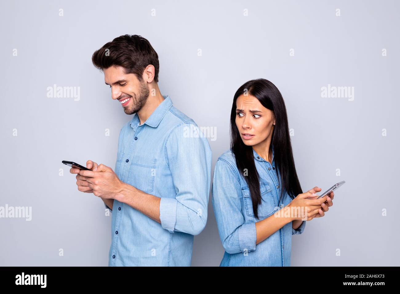 Profile side view portrait of nice attractive charming lovely couple holding in hands cell girl worrying, looking at guy's chat isolated over light wh Stock Photo