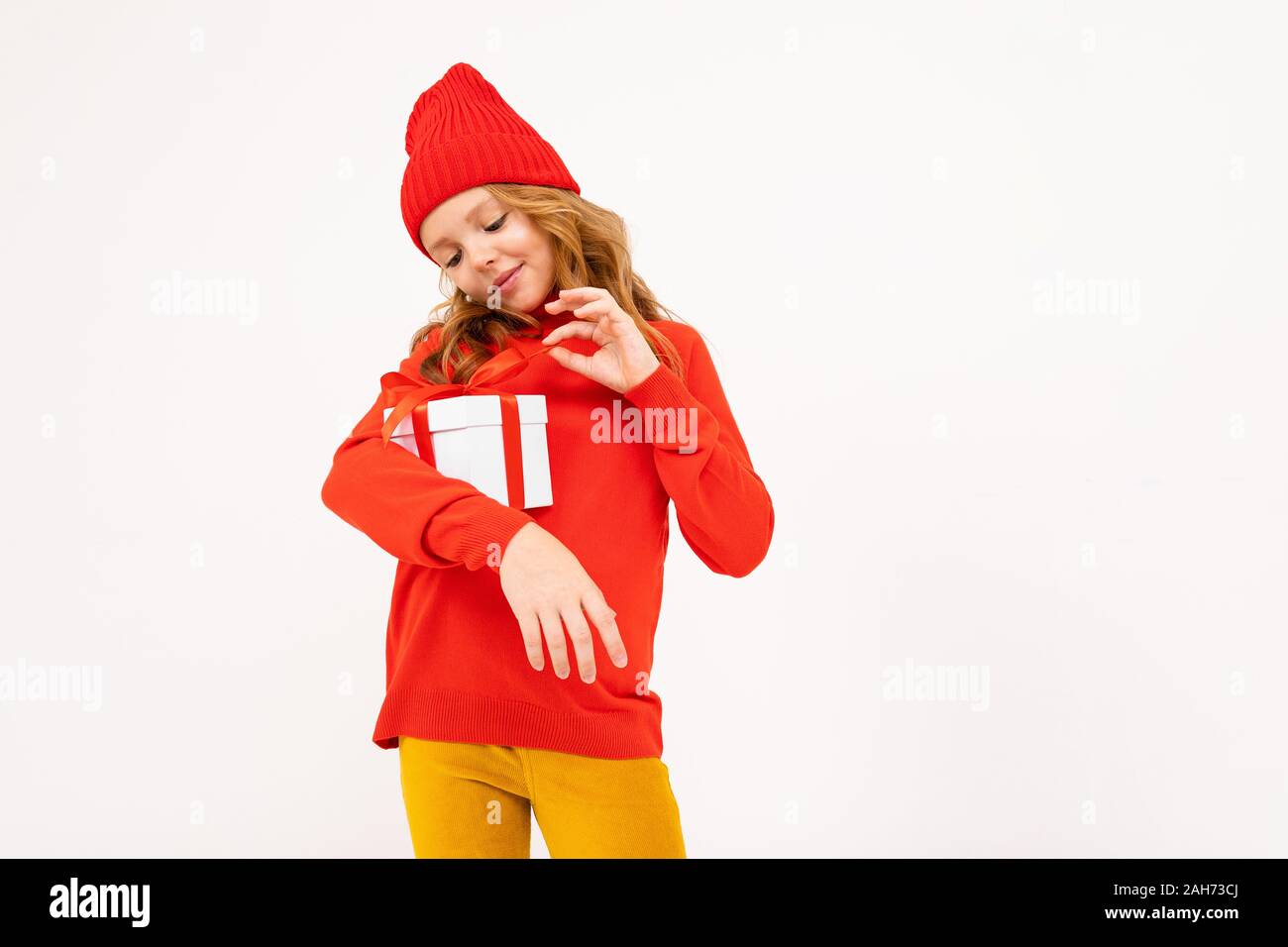 Little caucasian girl in red hoody and hat holds a white box with gift and has a lot of emotions isolated on white background. Stock Photo