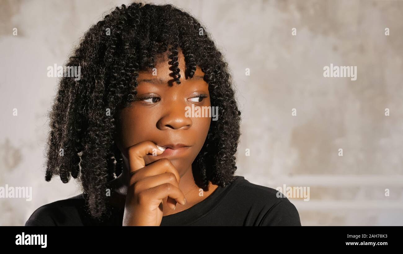 nervous black lady with fleecy hair holds finger on lips bites fingernails  and shakes head at white wall closeup Stock Photo - Alamy
