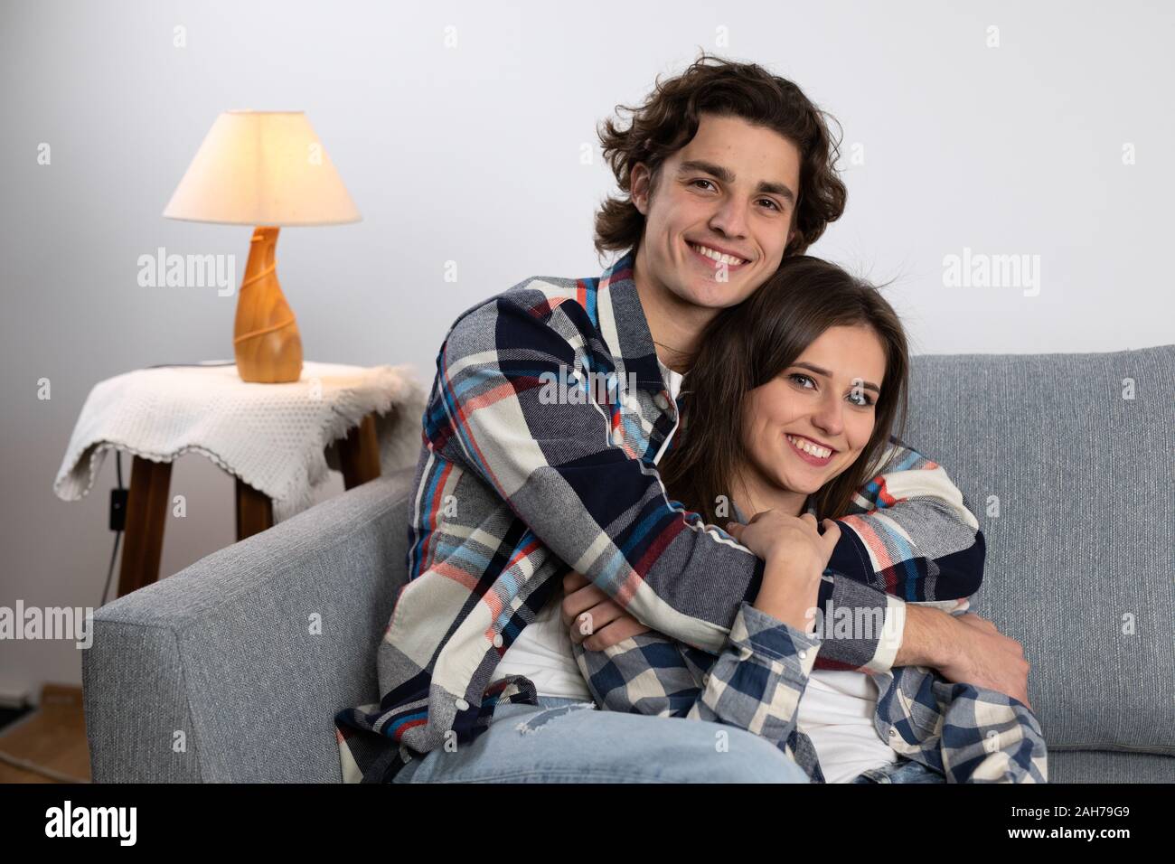 Smiling young man embracing girlfriend on couch. Stock Photo