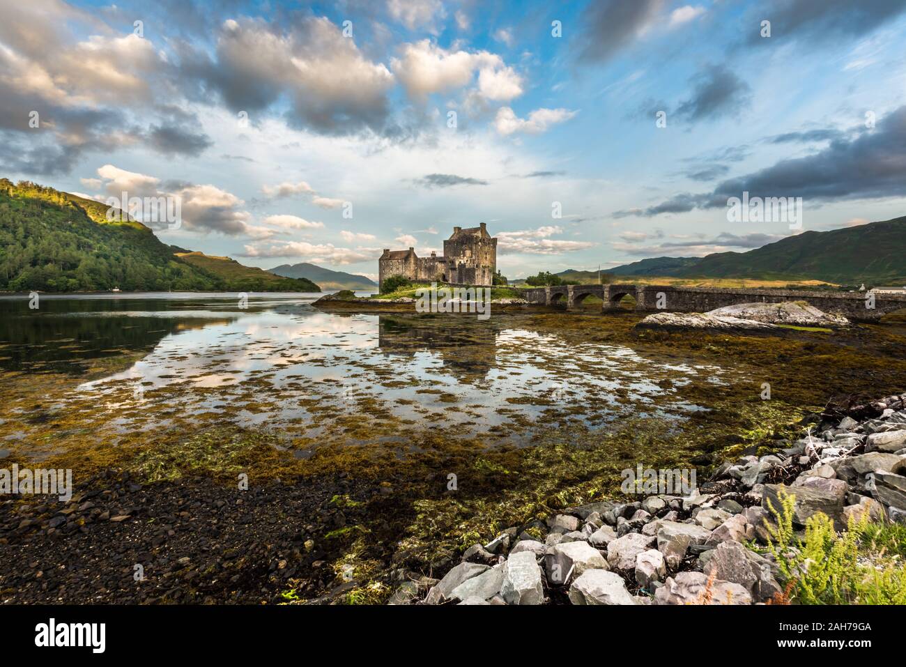 Ancient scottish castle sitting on a rock among seaweeds under a blue sky with puffy clouds in the early morning light Stock Photo