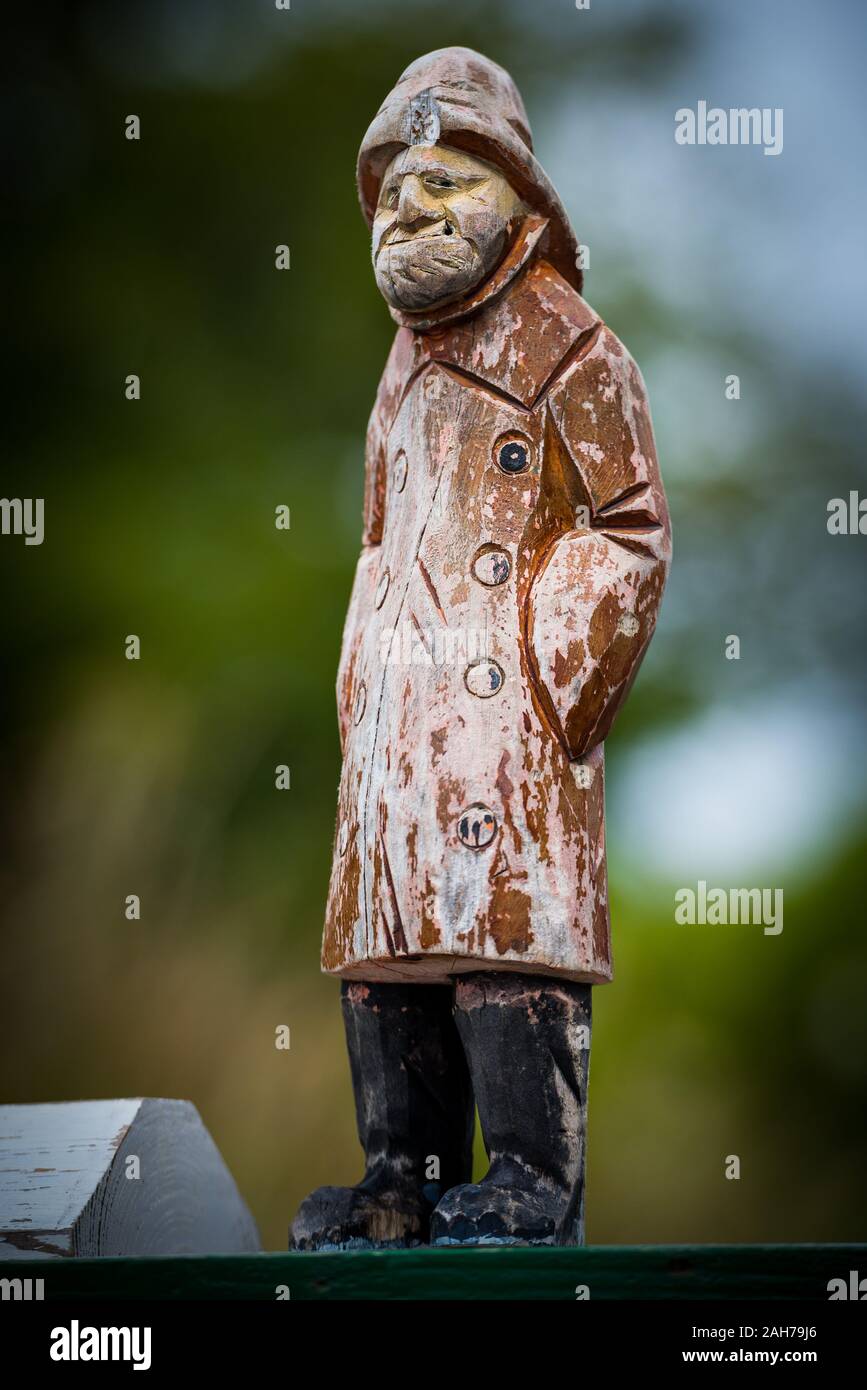 Close up of wooden representation of an old grumpy sailorman wearing a waterproof jacked and hood against a green bokeh background Stock Photo