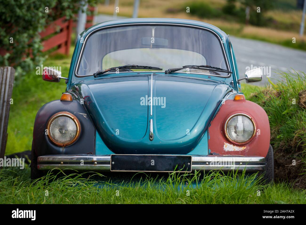 Front view of an old and battered light blue Volkswagen Beetle car, lying on the grass in a roadside junkyard Stock Photo